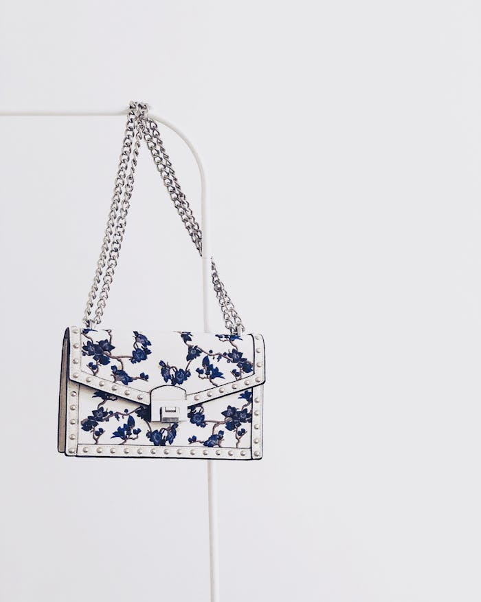 hero-services Elegant white handbag with blue floral design and silver chain, perfect for fashion enthusiasts.